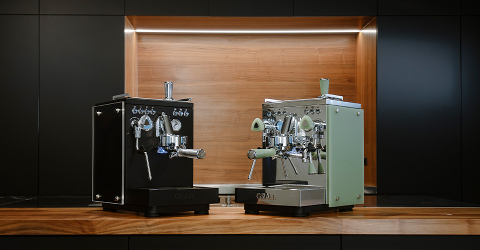 Zwei Espressomaschinen in Schwarz und Grün auf einer Holzoberfläche.