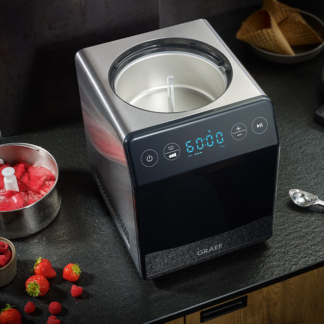 Eismaschine mit Früchten und Waffeln auf schwarzem Tisch