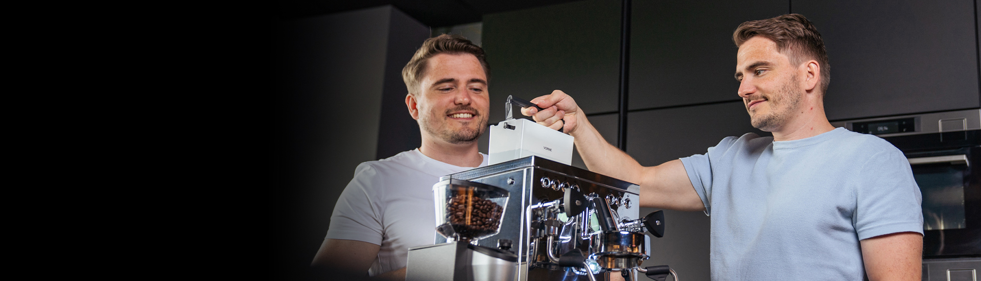 Due uomini che preparano il caffè. Sorridono e usano una macchina da caffè in cucina.