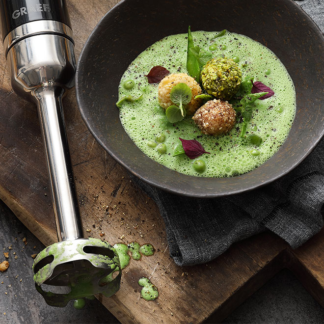 Grüne Suppe mit Bällchen, serviert in einer Schüssel, mit einem Stabmixer.
