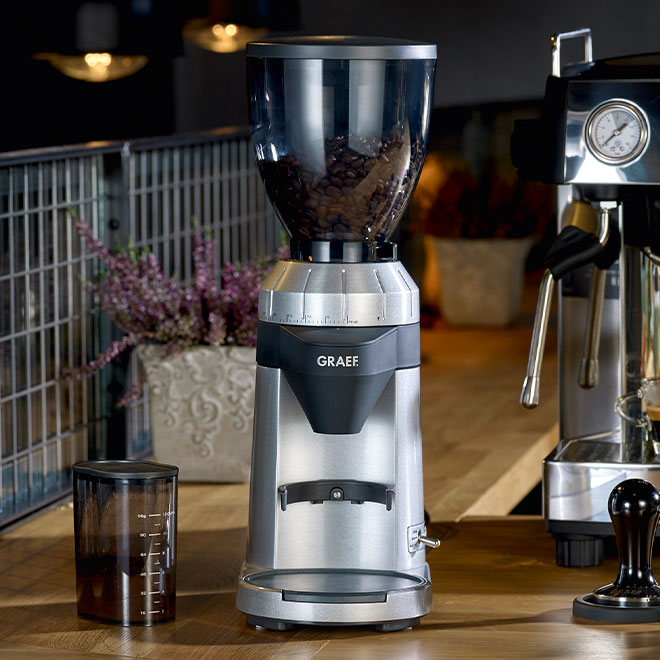 Kaffeemühle mit Bohnen, neben Espressomaschine und Zubehör auf Holzoberfläche