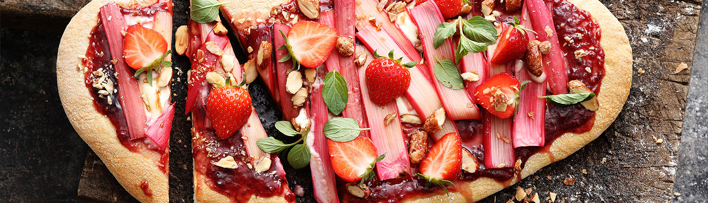 Strawberry rhubarb pizza with almonds and mint on a wooden surface
