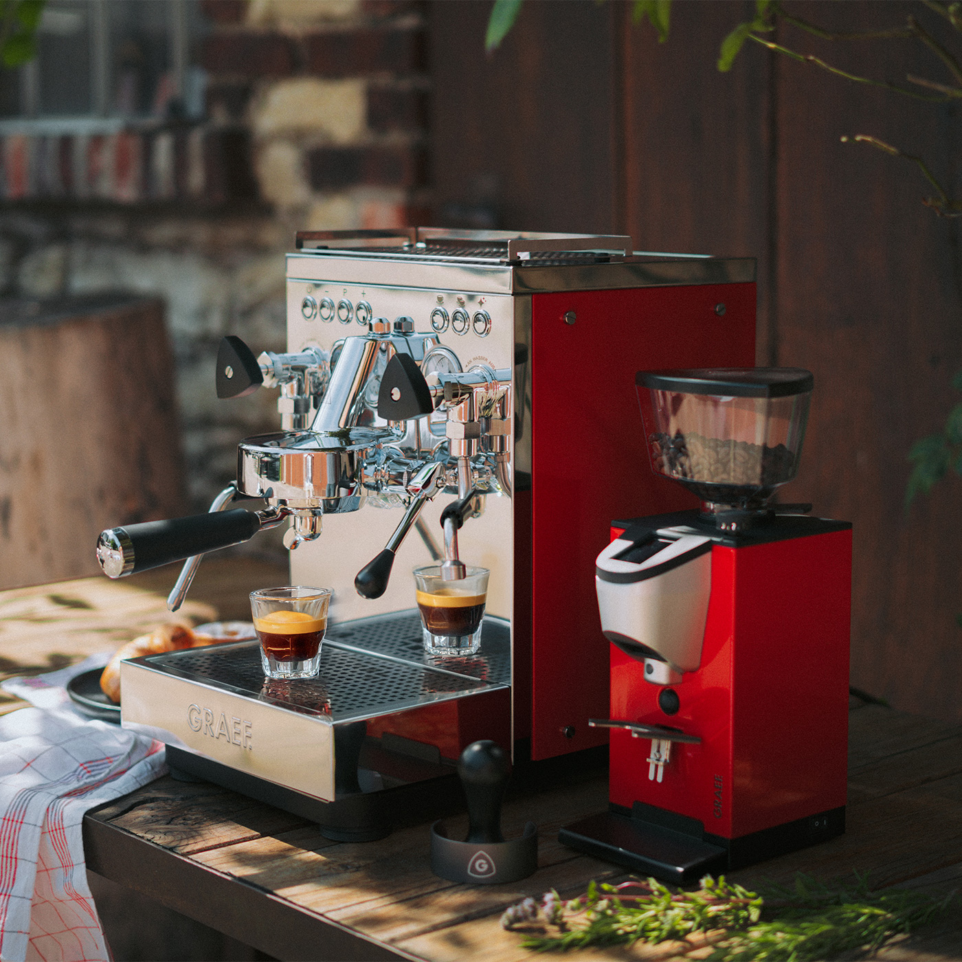 Eine rote Espressomaschine und ein Kaffee-Mühle mit zwei Espresso-Gläsern auf einem Holztisch.