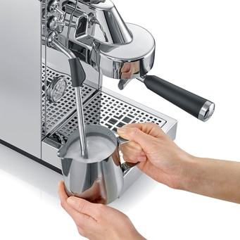 Milch aufschäumen in Milchkännchen mit silberner Siebträgermaschine, weißer Hintergrund