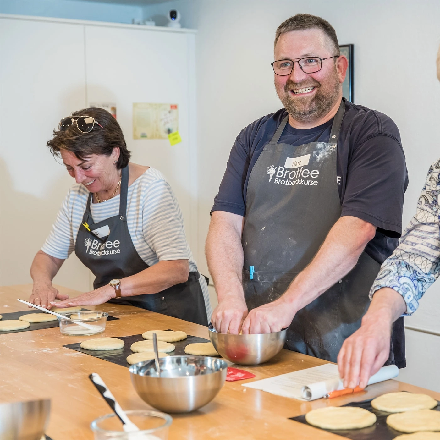 Bäckerkurs: Menschen backen Brot, lächeln und arbeiten zusammen am Tisch.