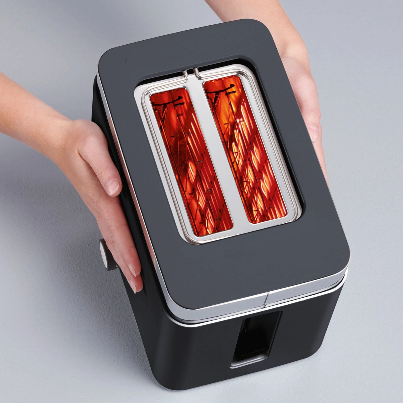 Toaster mit Händen gehalten, Innenansicht mit Heizdrähten, grauem Hintergrund.