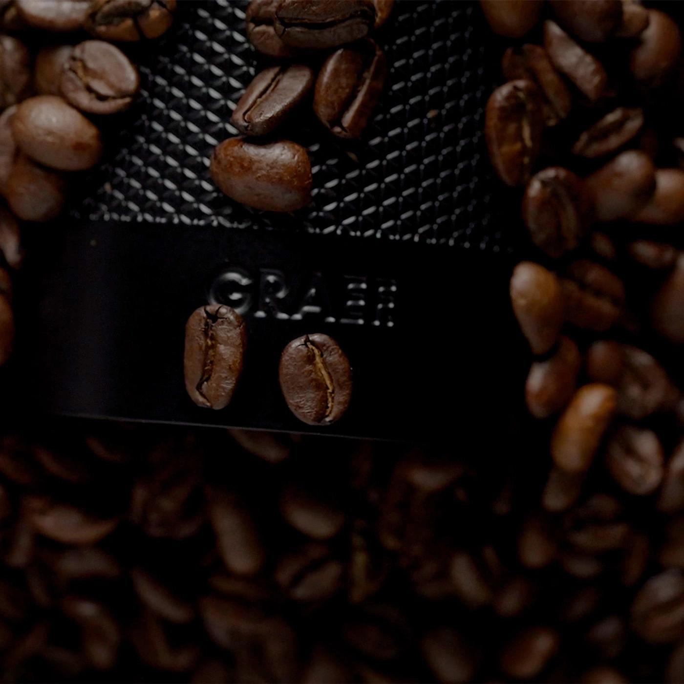 Geröstete Kaffeebohnen um eine Kaffeemühle mit dem Logo GRAEF.