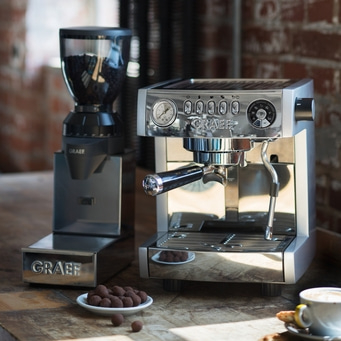 Kaffeemaschine und Kaffeemühle auf einem Holztisch mit Schokoladenkugeln.