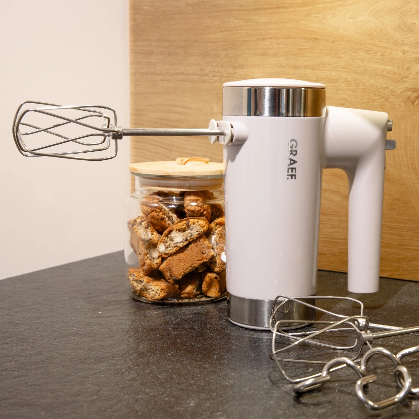 Handmixer mit Zubehör und Keksen in einem Glas auf einer dunklen Oberfläche