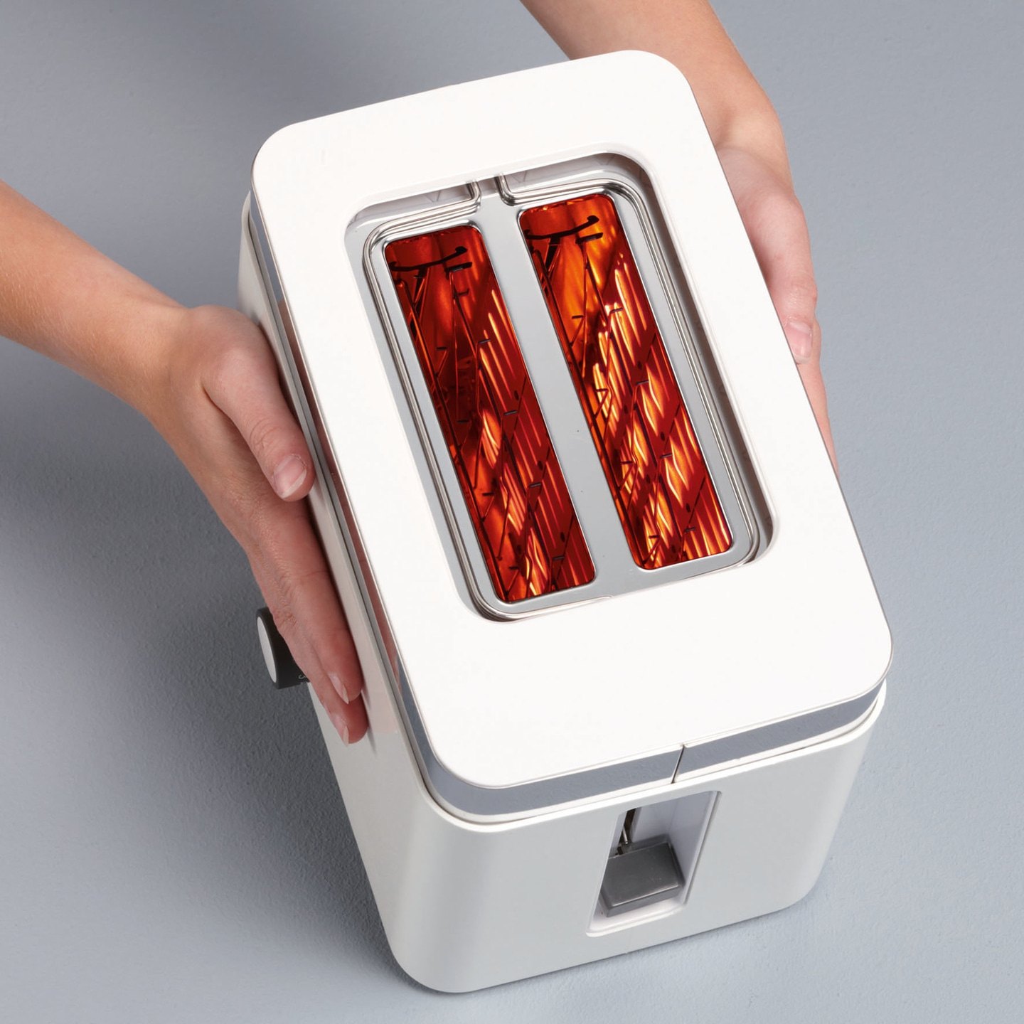 White toaster with red heating elements, held by hands, against a gray background.