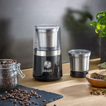 Kaffeemühle mit Zubehör und Kaffeebohnen auf Holzoberfläche.