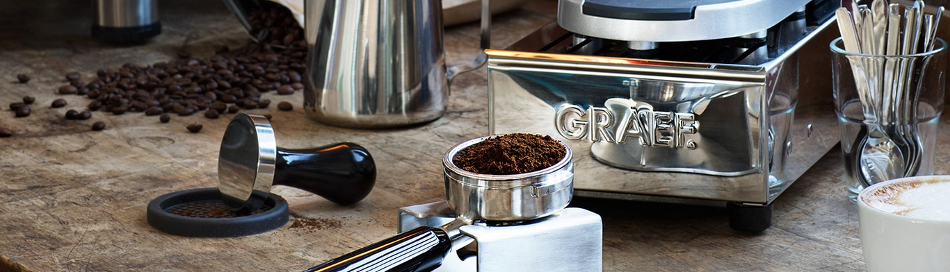 Kaffeemaschine mit Zubehör auf Holzoberfläche, Kaffeebohnen und Tasse.