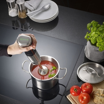 Handmixer in Topf mit Tomatensuppe, Basilikum, Tomaten und Kräutern auf Herdplatte