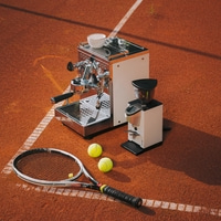 Kaffeemaschine und Tennisschläger auf Sandplatz