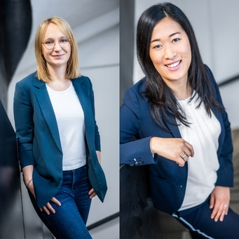 Zwei Frauen in Blazer posieren für ein Foto, lächelnd und selbstbewusst.