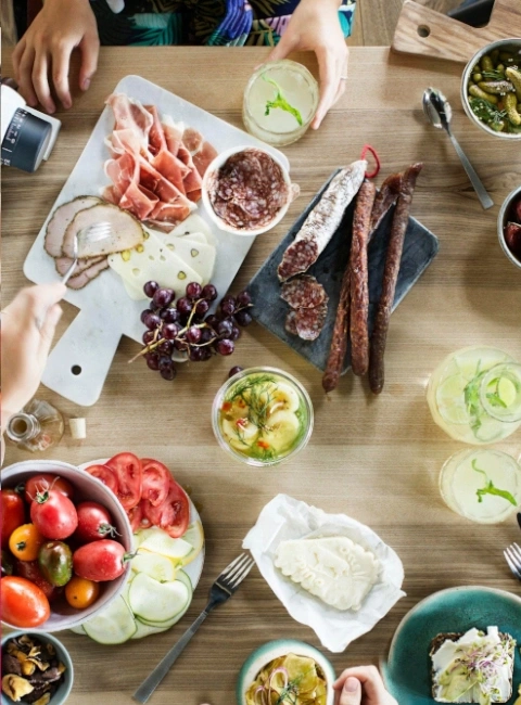 Tisch mit Essen: Wurst, Käse, Tomaten, Gurken, Trauben, Getränke, Menschen