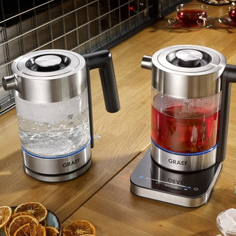 Zwei elektrische Wasserkocher auf einem Holztisch mit Tee und Dekoration.