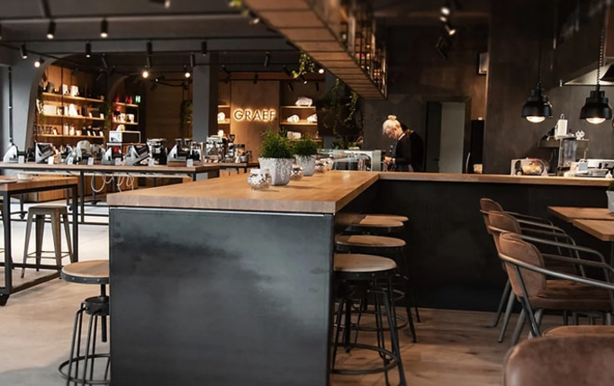 Un café avec des tabourets de bar, des tables et une personne travaillant derrière le comptoir.