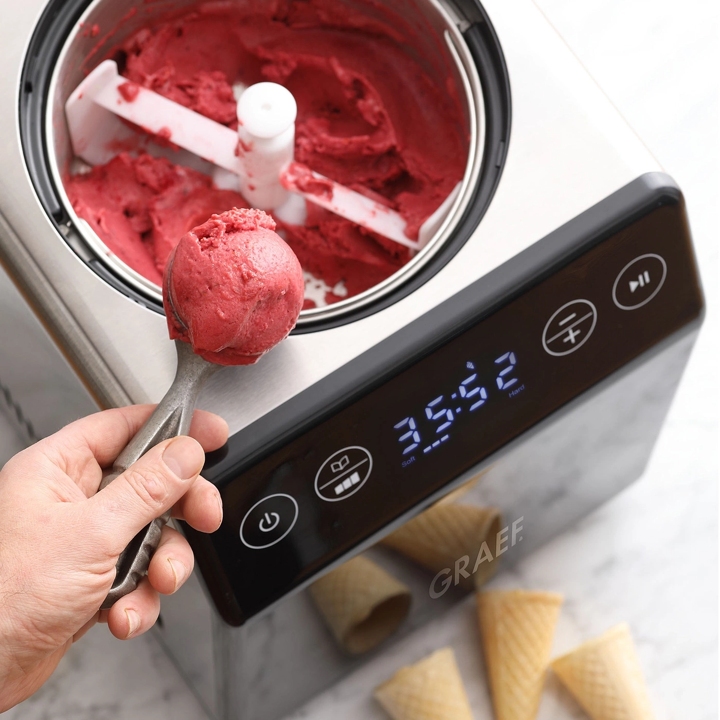 Eiscreme-Maschine mit roter Eiscreme, Eisportionierer und Waffelhörnchen.