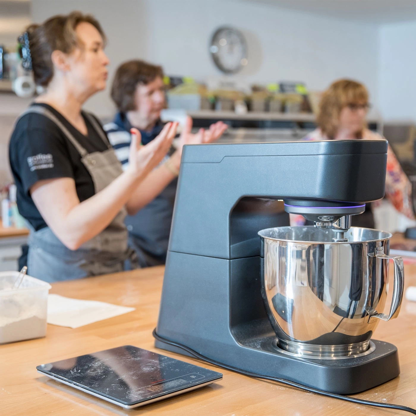 Küchenmaschine mit Personen im Hintergrund, die erklären und zusehen