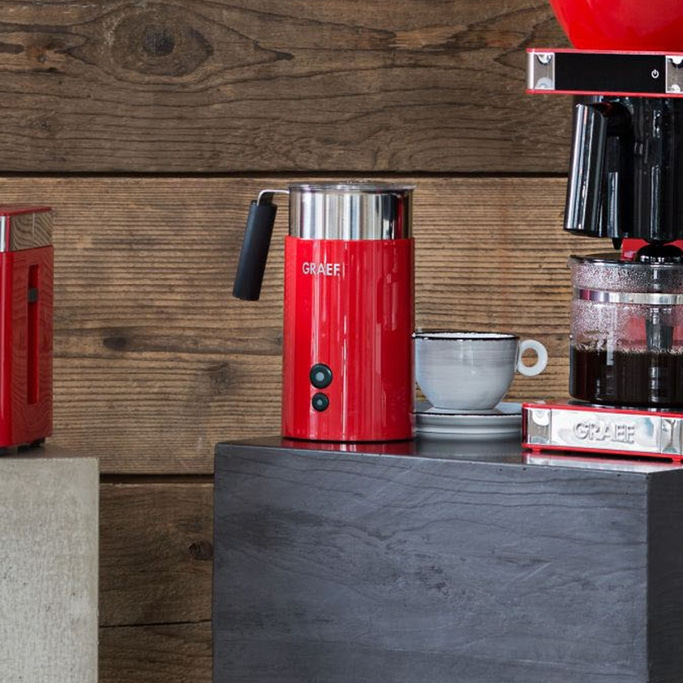 Red coffee machine and accessories on a dark table in front of wood