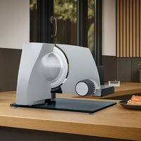 Grauer Fleischschneider auf Holztisch mit Essen im Hintergrund