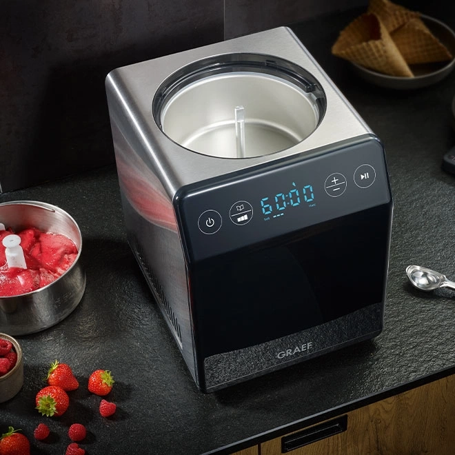 Eismaschine mit Früchten und Waffeln auf schwarzem Tisch