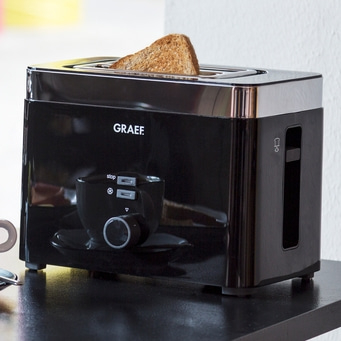 Schwarzer Toaster mit Toastbrot, Marke GRAEF, auf einer schwarzen Oberfläche.