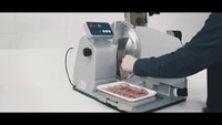 Meat slicer slicing salami. Person operating machine. Slices on tray. Silver machine.