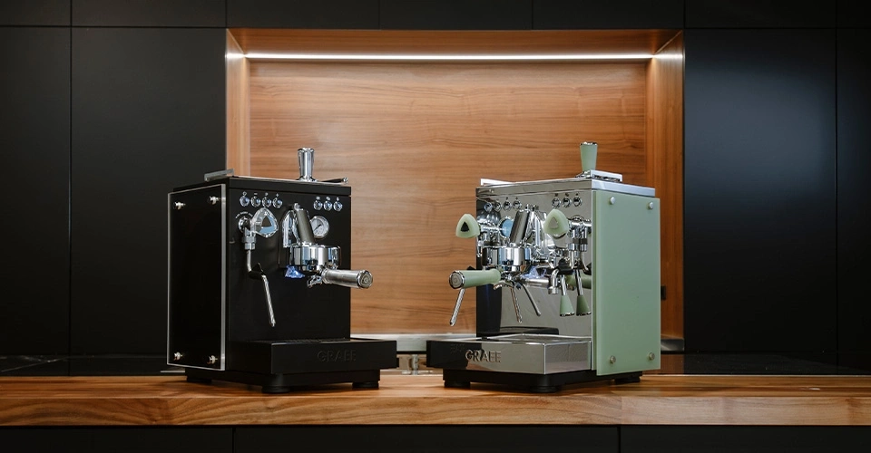 Zwei Espressomaschinen in Schwarz und Grün auf einer Holzoberfläche.