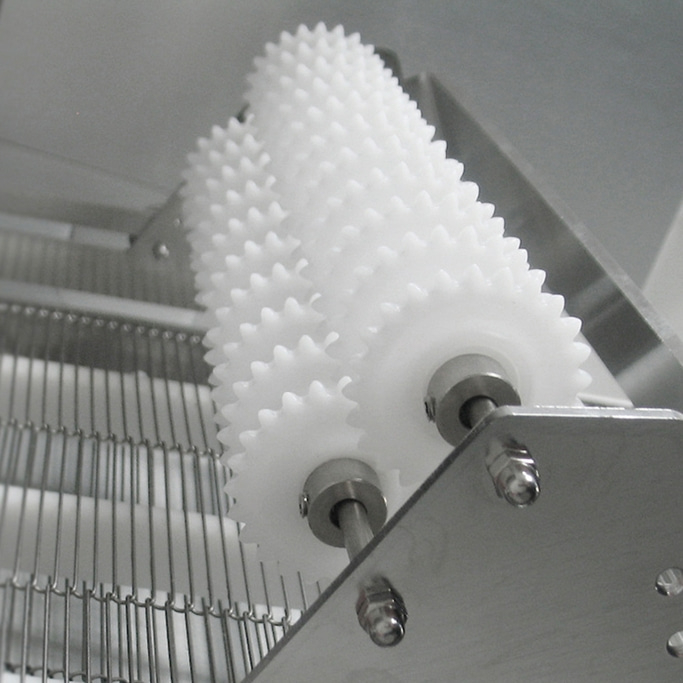 Zwei weiße Zahnräder mit Stacheln, die sich auf einer Metallplatte drehen.