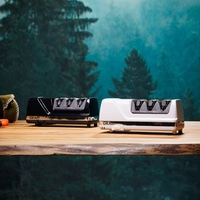 Zwei Messerschärfer, schwarz und weiß, auf einem Holztisch vor einem Waldhintergrund.