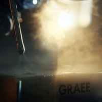 Dampfstrahl trifft auf eine Oberfläche mit Wassertropfen und dem GRAEF-Logo.