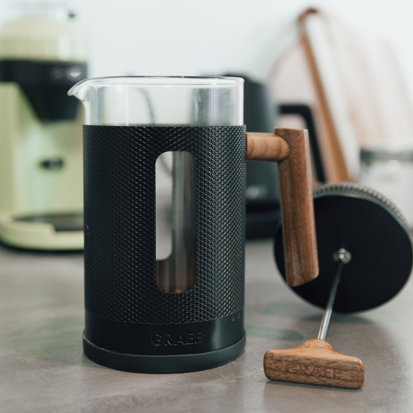 Presse à café avec manche en bois et boîtier noir sur une surface grise, gros plan.