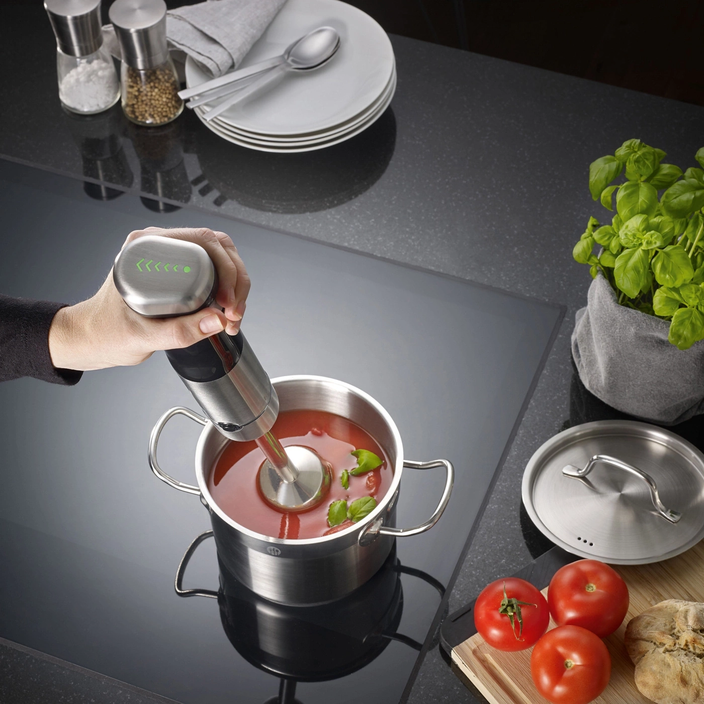 Handmixer in einem Topf mit Tomatensuppe, Zutaten und Kräutern