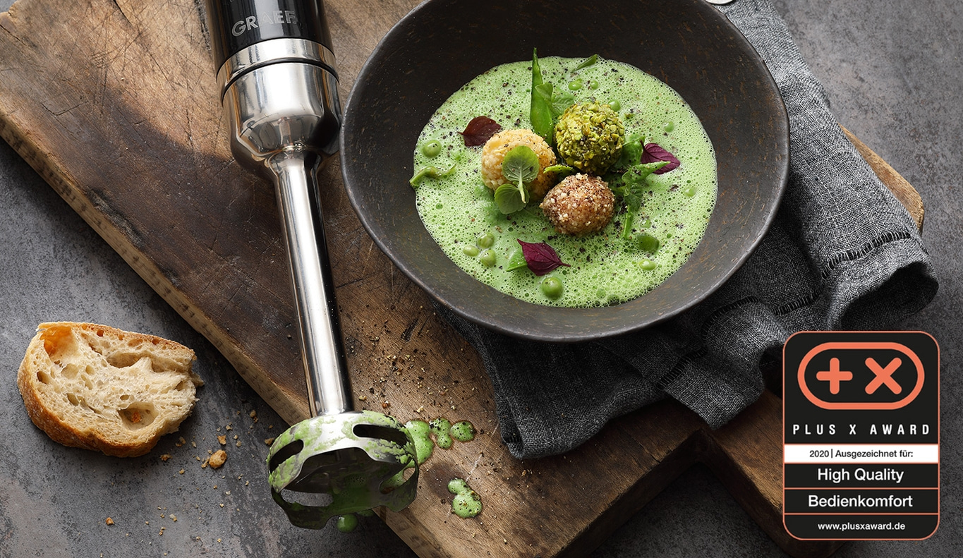 Zuppa con erbe e pane, accanto a un frullatore a immersione, premiato con il Plus X Award.