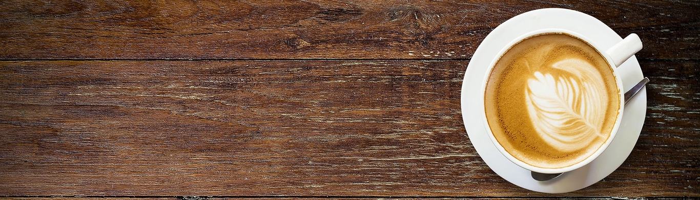 Caffè su legno, con latte art, su un piattino, con cucchiaio, visto dall'alto