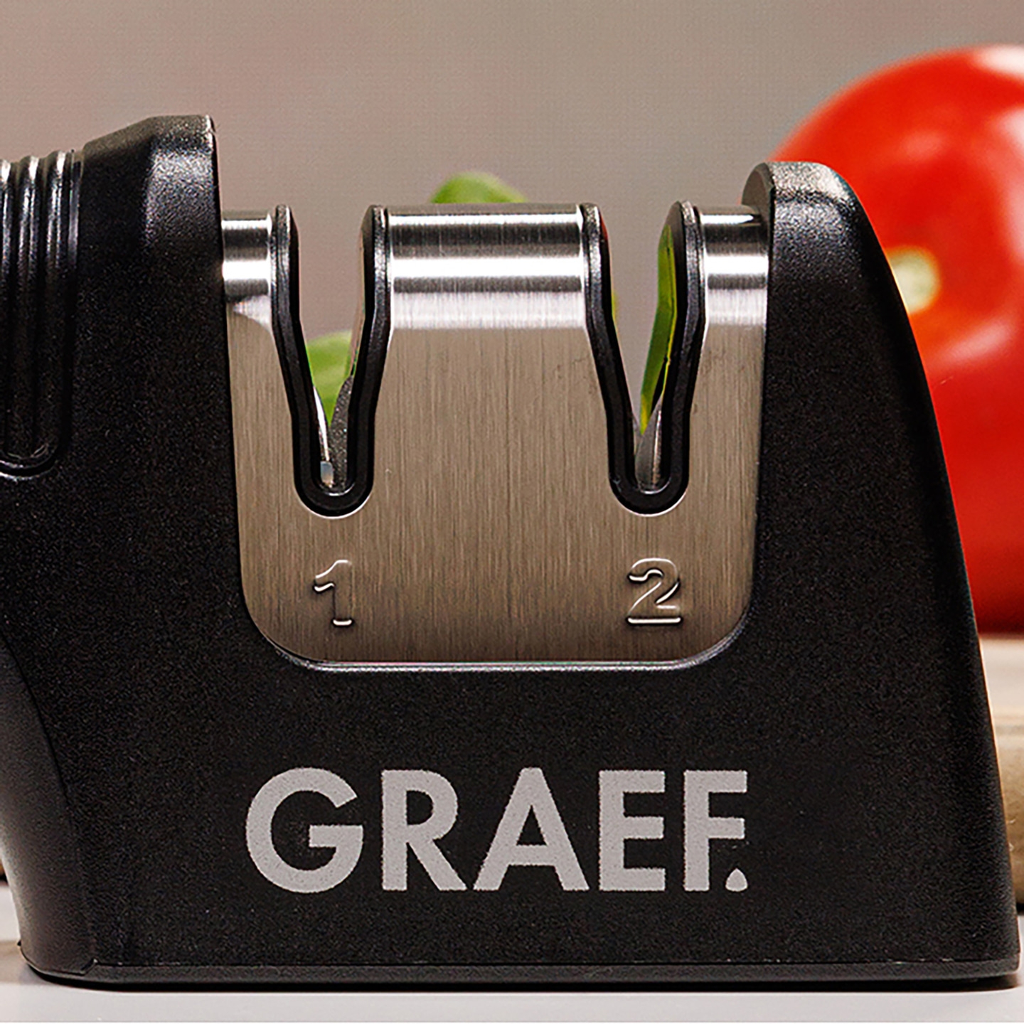 Ein Graef Messerschärfer mit den Zahlen 1 und 2, daneben ein roter Tomate.