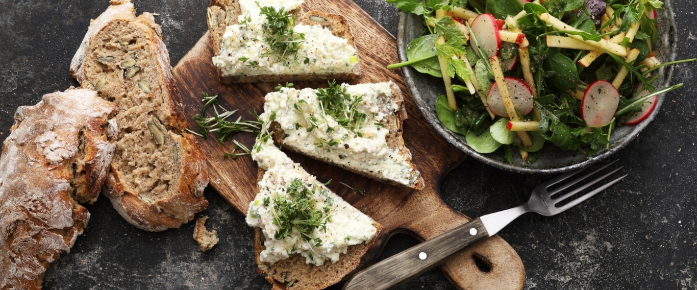 Brot mit Frischkäse und Salat auf einem Holzbrett, rustikal
