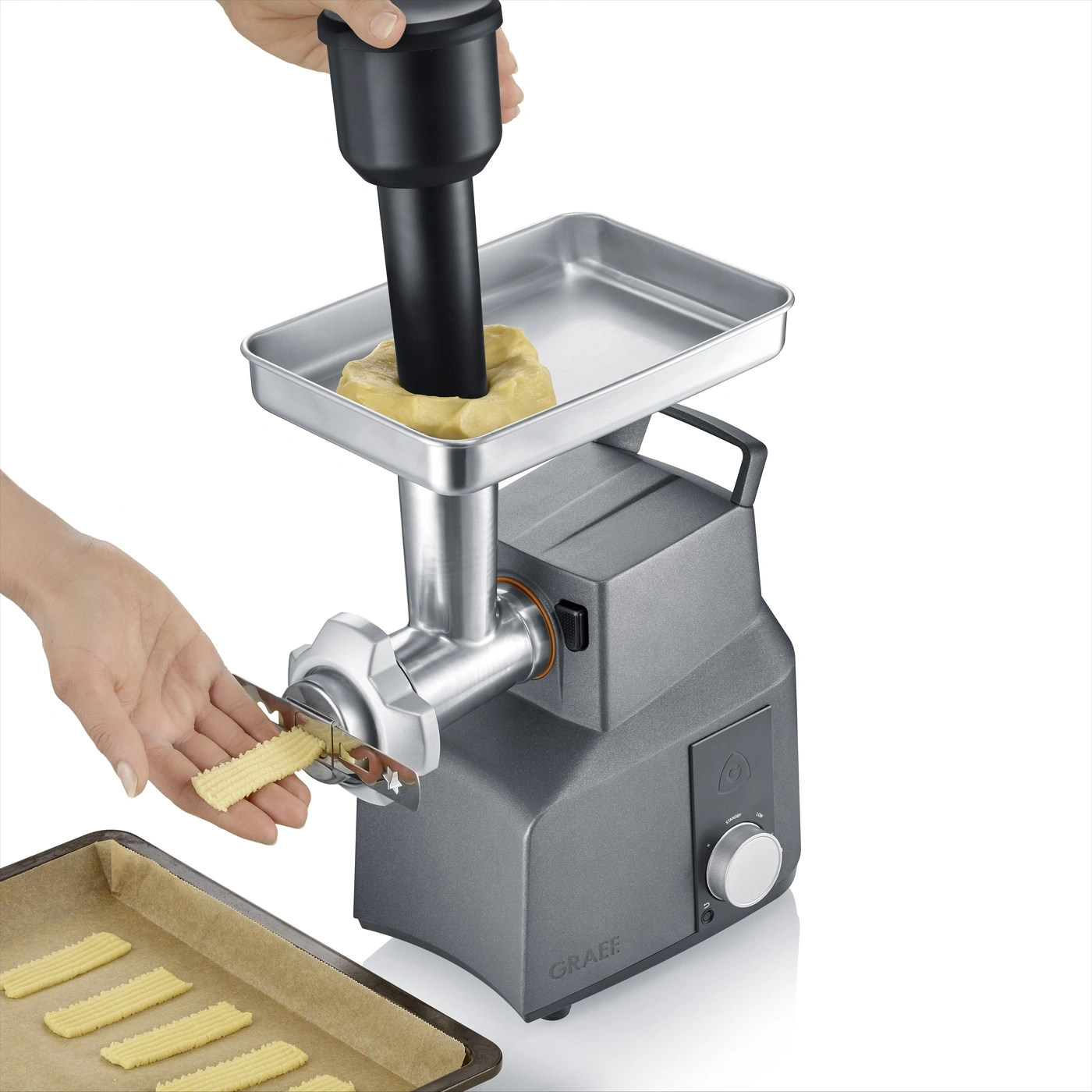Eine Hand drückt Teig in eine Gebäckpresse, die Kekse auf ein Backblech formt.