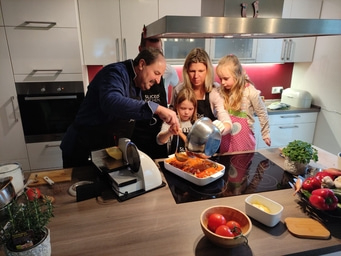Familie kocht gemeinsam in der Küche, gießt Soße in Auflaufform.