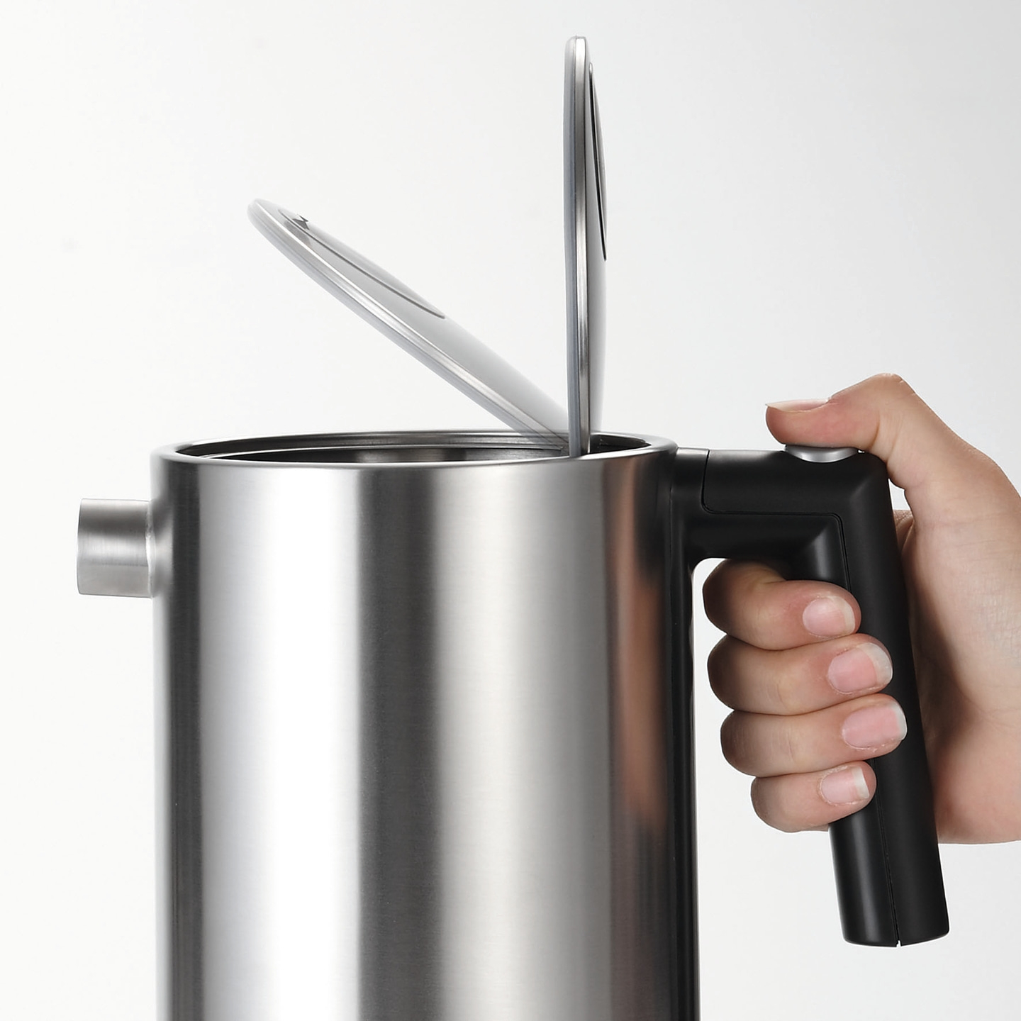 Stainless steel kettle with open lid and handle held by a hand, close-up shot.