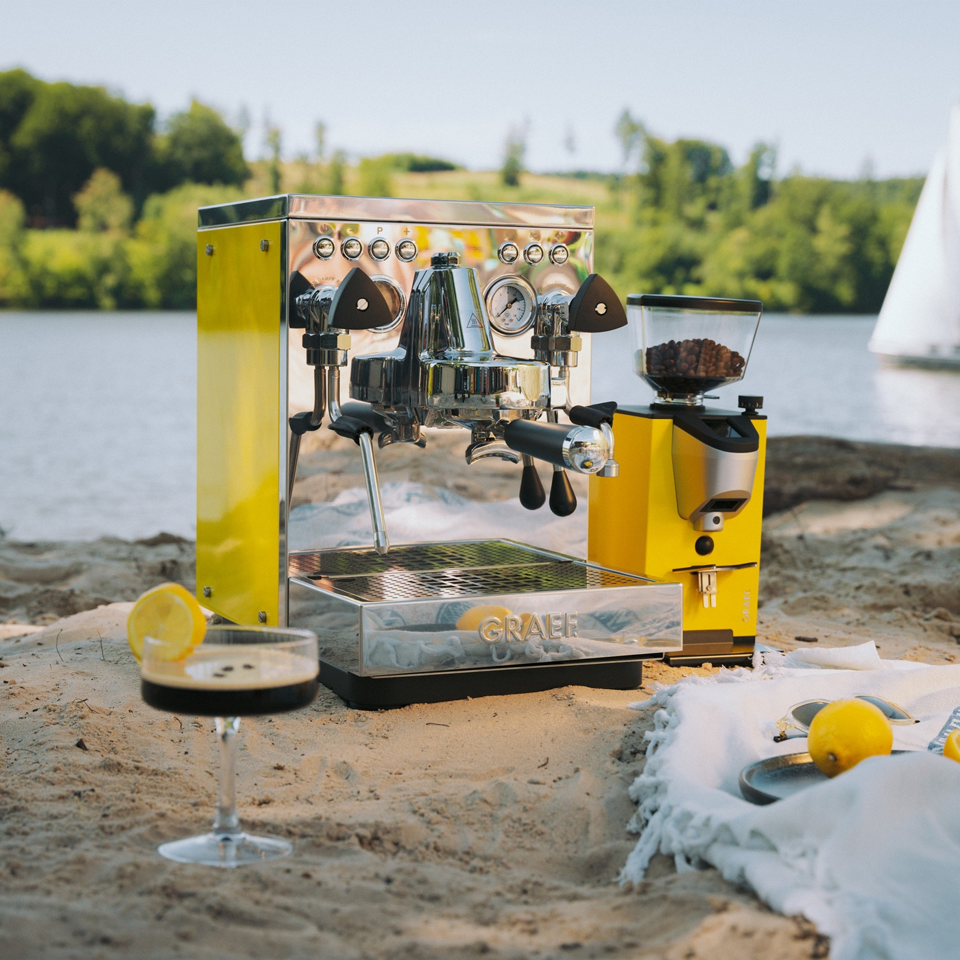 Eine gelbe Espressomaschine und Kaffeemühle am Strand mit einem Getränk.