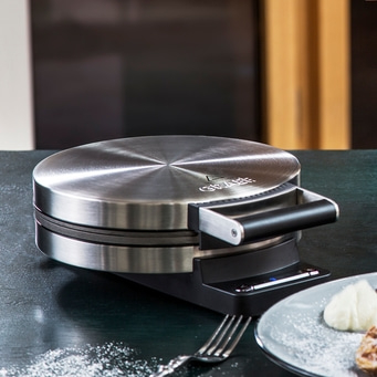 Macchina per waffle sul tavolo con waffle e forchetta, primo piano
