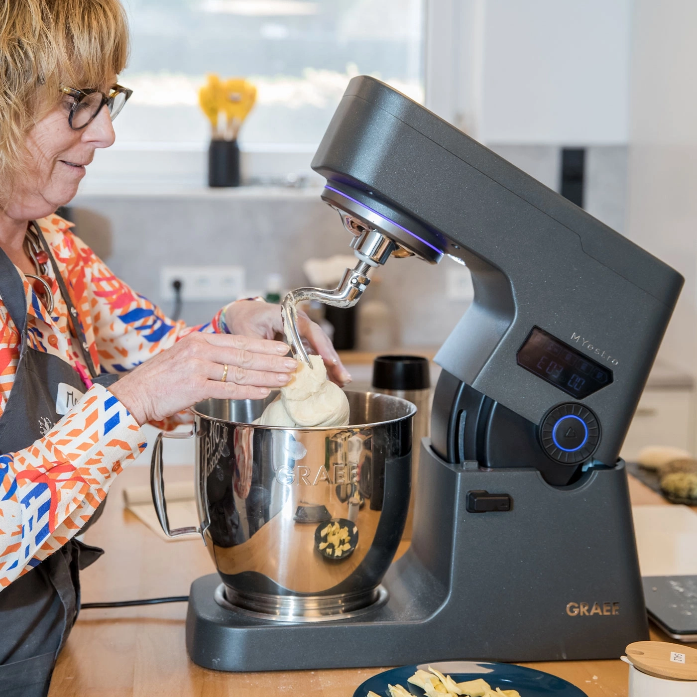 Frau benutzt Küchenmaschine, um Teig zu kneten, in einer Küche.