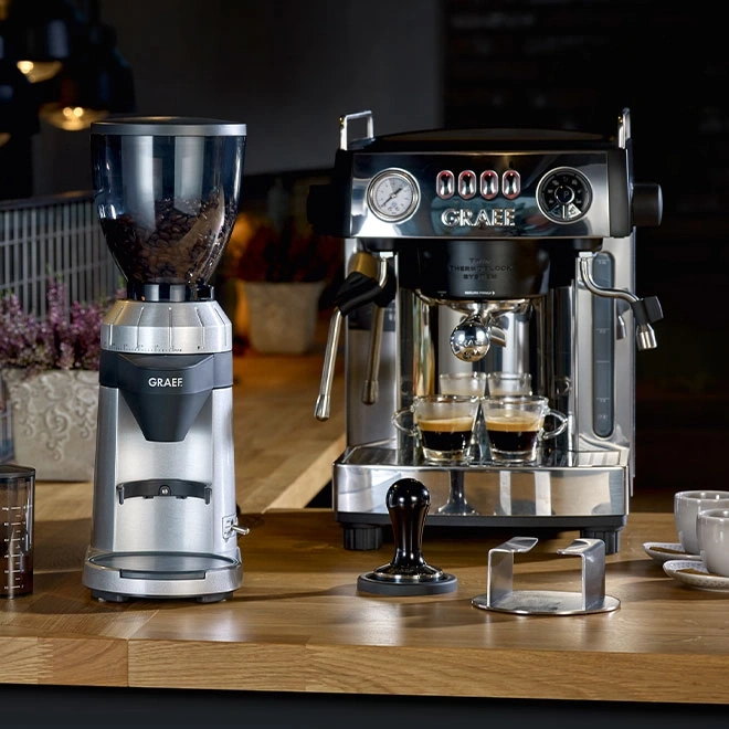 Kaffeemaschine und Kaffeemühle auf einer Holzoberfläche mit Zubehör.