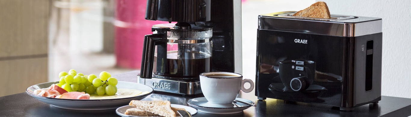 Scène de petit-déjeuner avec café, toasts et fruits sur une table.