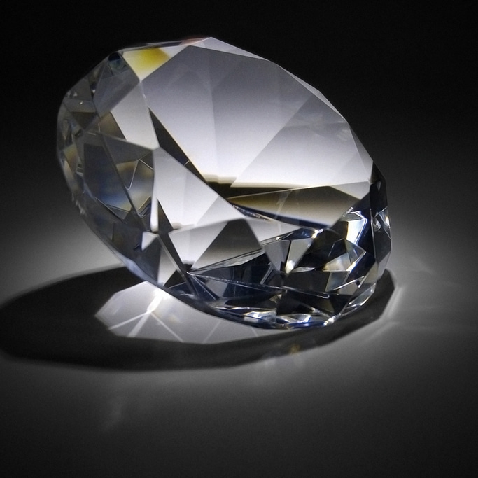 Ein Diamant, der auf einer dunklen Oberfläche liegt und Licht reflektiert.
