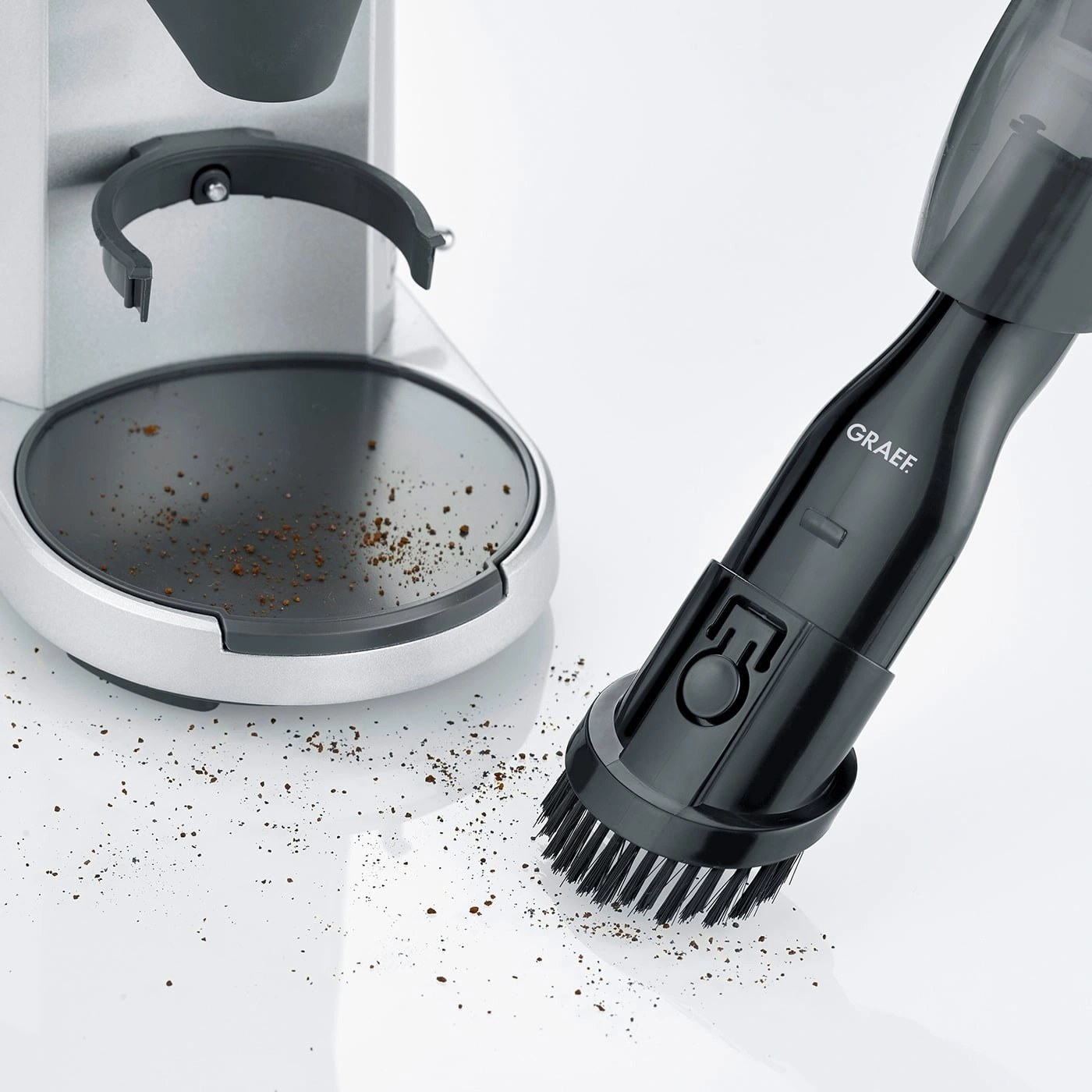 Kaffeemühle und Staubsauger mit Bürste reinigen Kaffeepulver auf weißem Untergrund.