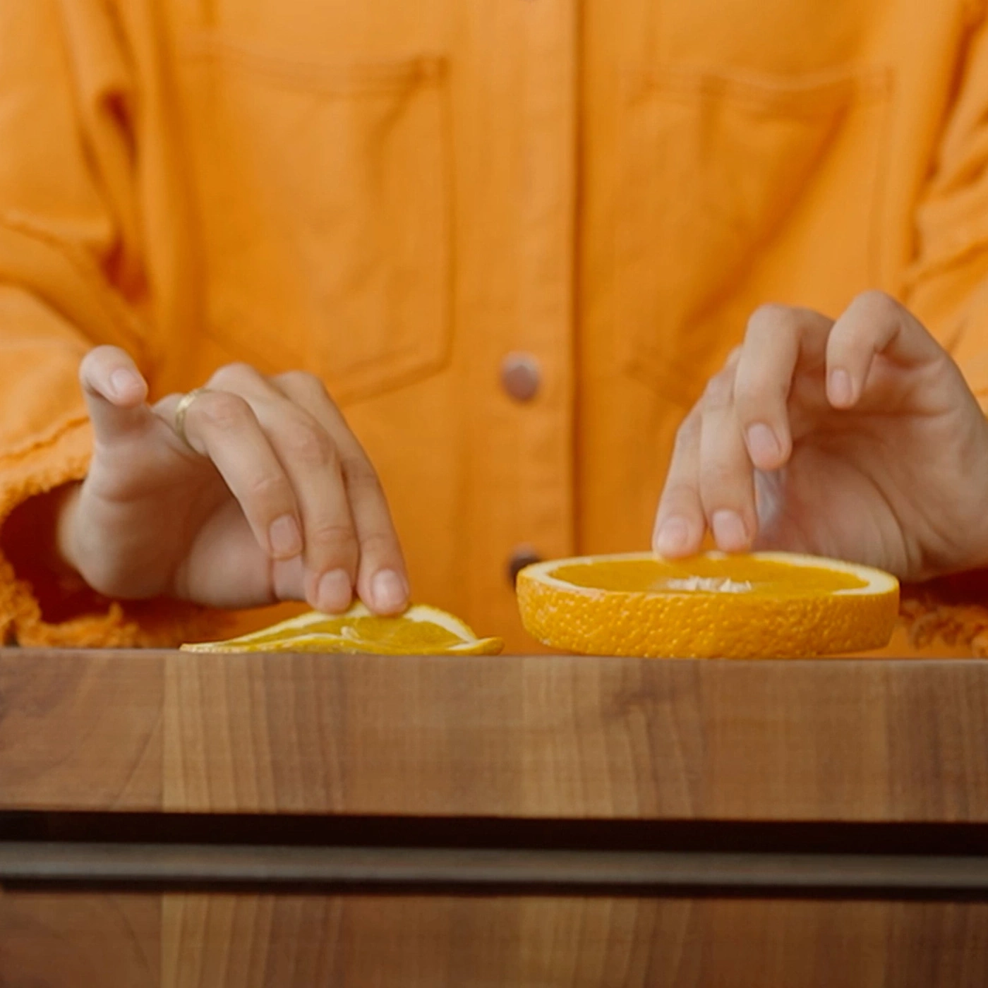 Person arrangiert Orangenstücke auf einem Holztisch, ein dünnes und ein dickes Stück.